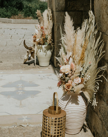 vintage ceramic floor vases with dried floral & pampas arrangements, wicker lantern & candle, and a vintage rug to adorn a wedding ceremony space. All items described are for rent in Winnipeg & surrounding towns in Manitoba.