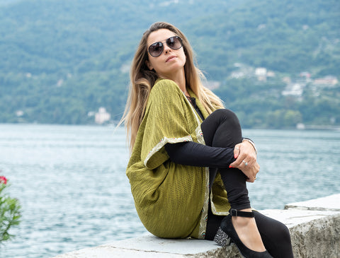 La nostra modella indossa il cardigan Khomal - Verde lime sopra un completo nero, mentre siede su un muretto in riva al lago.