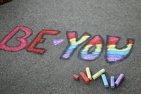 Chalk lettering spelling out 'Be You' with rainbow colors in the word 'You'.