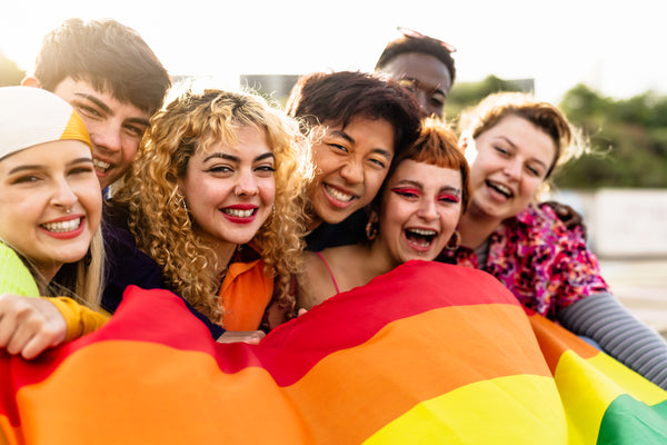 Young adults and teens of diverse backgrounds holding a rainbow pride flag