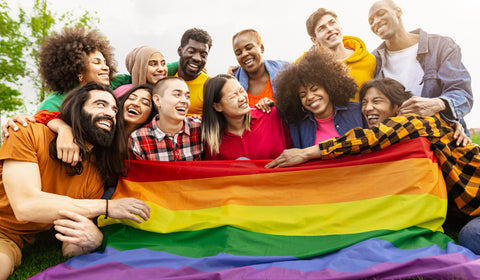 Crowd of happy diverse young friends celebrating Pride with a LGBTQ+ Rainbow Pride Flag.