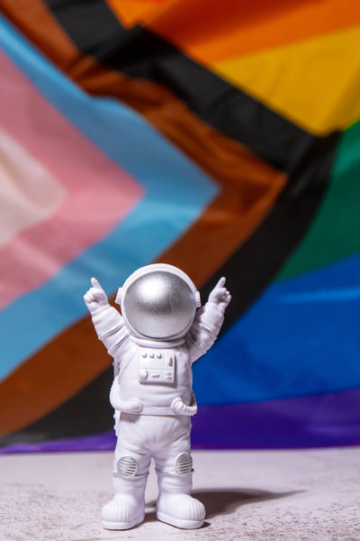 Toy astronaut in victory pose in front of Inclusive Pride Flag background | LGBTQ Pride