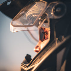A motorcyclist wearing white sunglasses looking out at a sunset