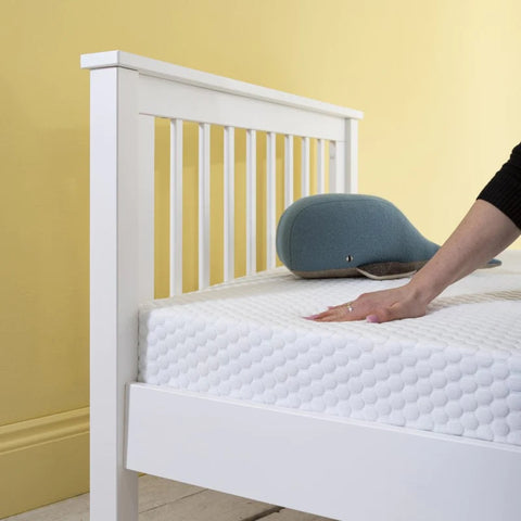 a white mattress with a soft toy whale on top and someone's hand pressing down on it