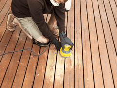 quelqu'un en train de sabler une terrasse en bois pour changer de couleur de teinture