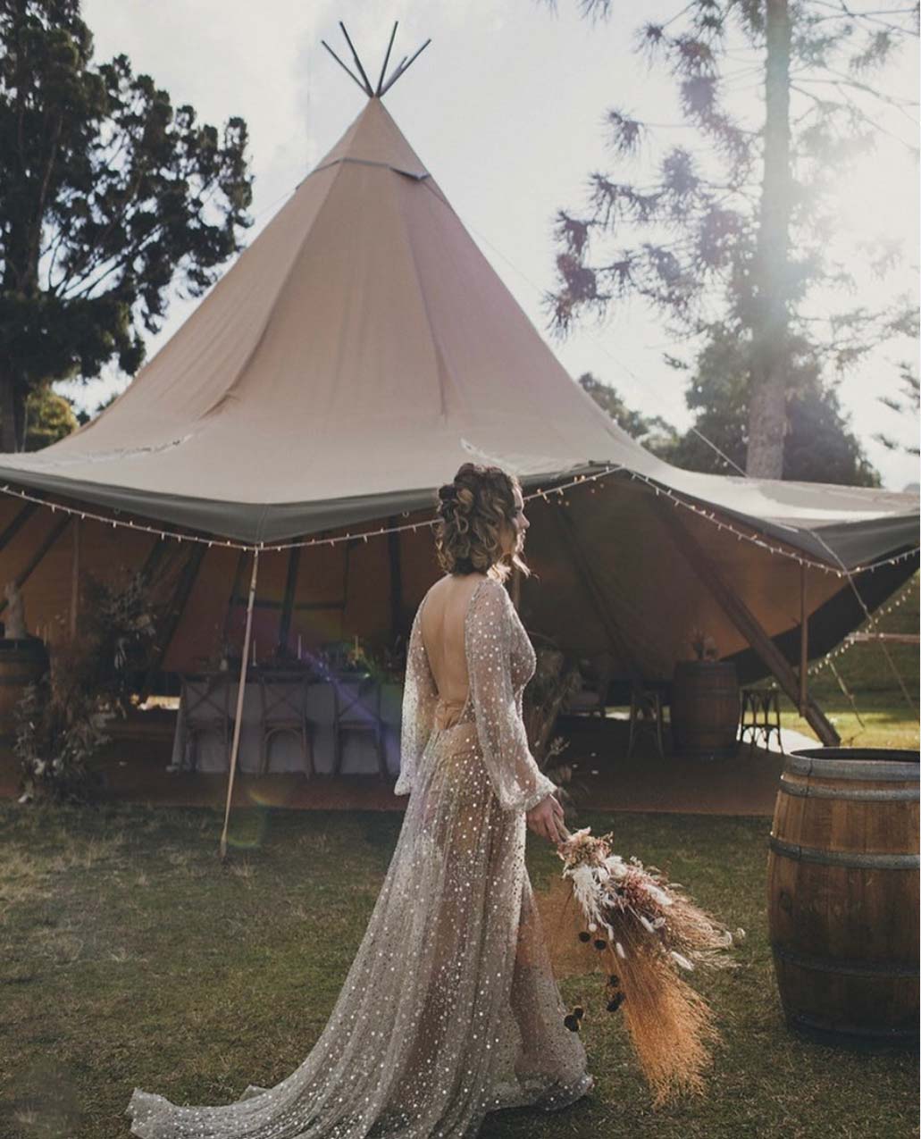 Ecru translucent wedding gown with elegant sparkles, bride with a teepee at a boho wedding