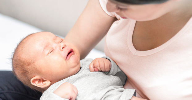 Eine Frau hält ein weinendes Baby mit schmerzverzehrtem Gesicht auf dem Arm.