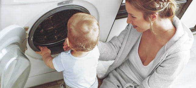 Mutter und Kleinkind stehen gemeinsam vor der geöffneten Waschmaschine