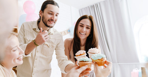 Paar mit Freunden feiert eine Gender Reveal Party mit Cupcakes.