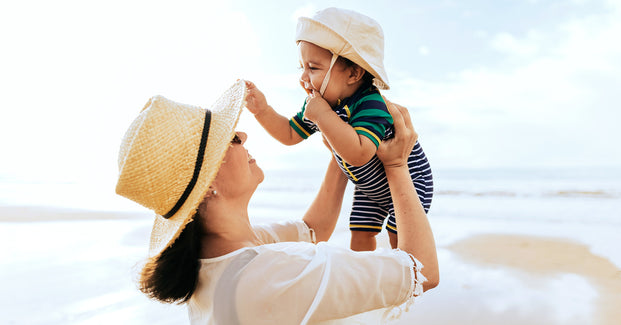 Mutter mit Baby mit Sonnenhut am Strand.