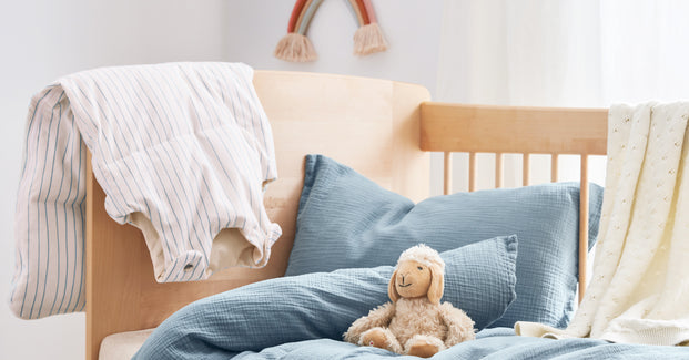 Musselin Bettwäsche, ein Schlafsack und ein Kuscheltier liegen auf einem Kinderbett.