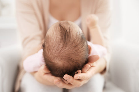  Mutter hält Baby auf den Knien, das Köpfchen mit der Fontanelle ruht in ihren Händen. 