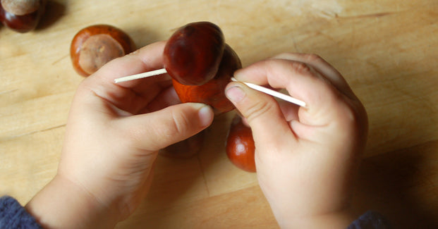 Kinderhände basteln ein Kastanienmännchen mit Zahnstochern