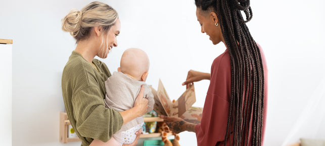 Zwei Mamas schauen sich mit ihrem Baby ein Bilderbuch an