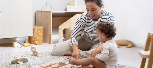 Mutter und Kind sitzen gemeinsam auf dem Kinderzimmerboden und spielen.