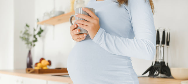 Schwangere Frau hält eine Tasse Himbeerblättertee in der Hand.