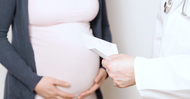 Schwangere Frau hält sich ihren Babybauch und wird von einem Arzt beraten.