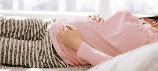 Schwangere Frau liegt auf dem Bett und streichelt ihren Bauch