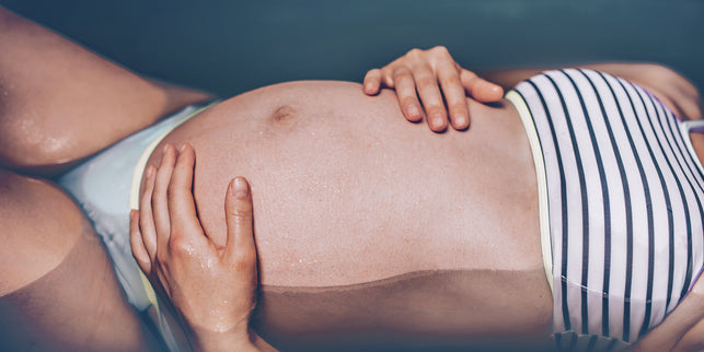 Schwangere Frau im Bikini liegt im Wasser.