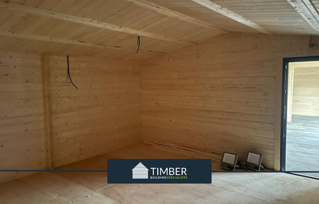 First internal view of the log cabin, highlighting the spacious office room with dark grey laminate flooring."