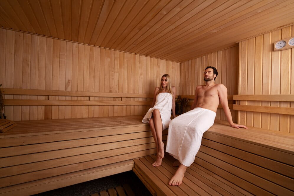 man and woman clad in towel relaxing inside a sauna