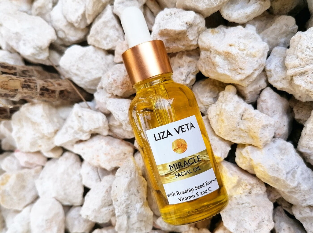 Natural facial oil in a clear glass bottle with a dropper on white stones.