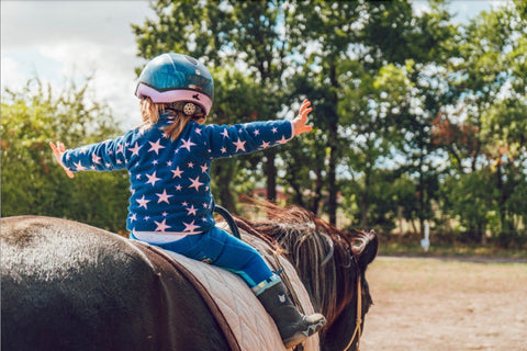 Kind reitet auf Pferd und streckt Arme aus