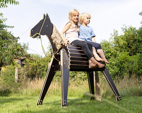 Zwei Kinder sitzen auf Holzpferd im Garten