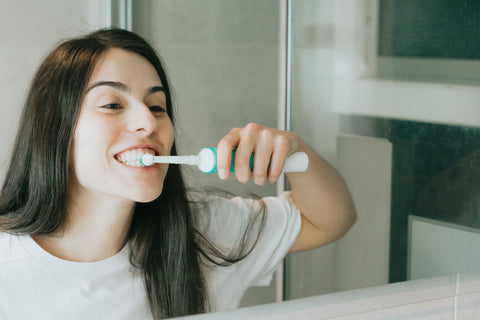 Een jonge vrouw met een lichte huid en donker loshangend haar is haar tanden aan het poetsen.