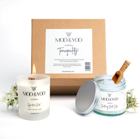 A studio shot of our tranquility gift set with our signature scented candle on the right and our soothing bath salts on the left, both placed infront of the natural gift box.