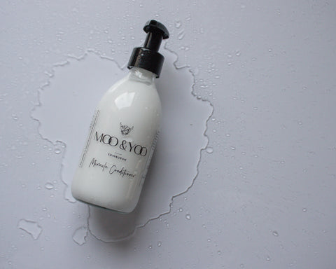 A bottle of Moo & Yoo Miracle Conditioner lying on a white surface in a puddle of water.