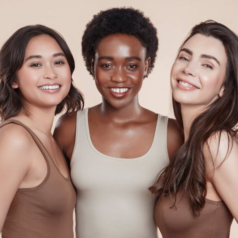 Three female models with moo and yoo products in their hair all wearing jeans and neutral coloured vest tops. They are looking directly at the camera. All have glowing skin and healthy shiny hair. One girl with bob length wavy hair, One with black natural textured hair and one with long brown hair. Model with long flowing brunette hair. She has super shiny hair with lots of volume. They have all used Moo and Yoo Miracle Conditioner.