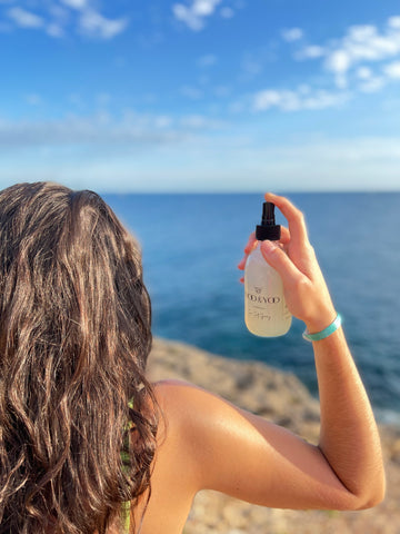 spraying sea salt spray into brunette hair on the cliffs next to the ocean