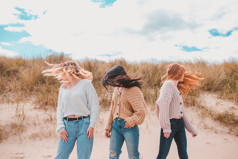 Three models (blonde hair, brown hair and red hair) on the beach. Their heads are turned and their hair is flowing in the wind.