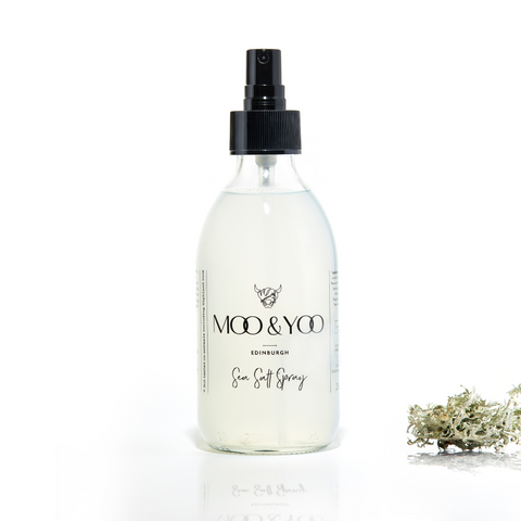 A glass bottle of Moo and Yoo Sea Salt Spray Milk with a spray lid on a white background with a sprig of Icelandic moss placed to one side