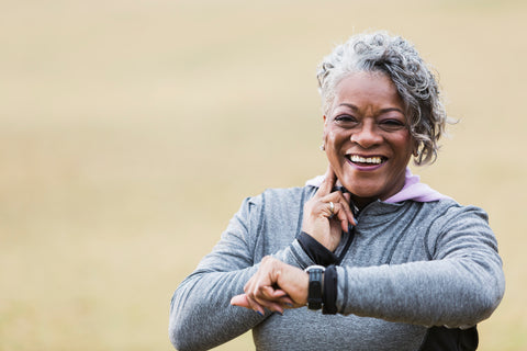 African American senior woman (60s) exercising outdoors, taking pulse and laughing