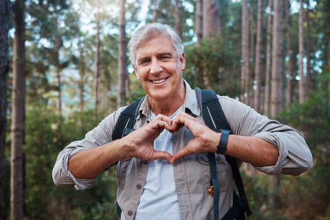 Senior Man Walking in Woods Showing Healthy Heart Hand Symbol