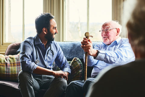 Young male doctor and senior man sitting on sofa and smiling during home visit