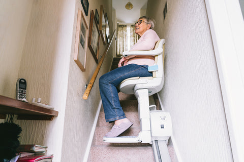 Senior woman using automatic stair lift on a staircase at her home. Medical Stairlift for disabled people and elderly people in the home.