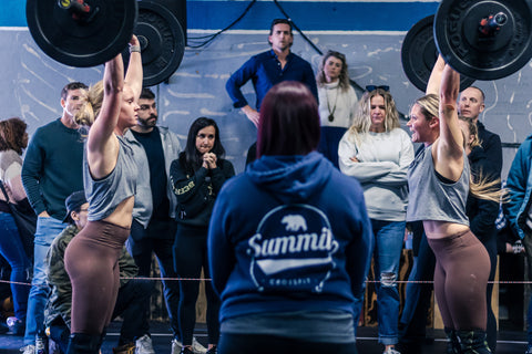 Two female athletes pressing a barbell overhead