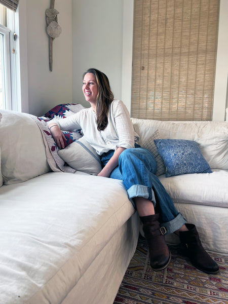 Portrait of Aster House Co-Founder Emily Rives sitting on a white linen sofa in premium denim and blouse.