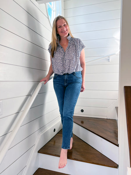 Portrait of Aster House Co-Founder Randa Blair standing in a stairwell wearing premium denim and floral blouse