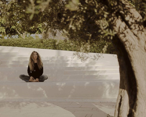 Ani Han, Enso Design Lab’s creative director, seated in a meditative pose under the shade of trees, showcasing a moment of tranquility and connection with nature.