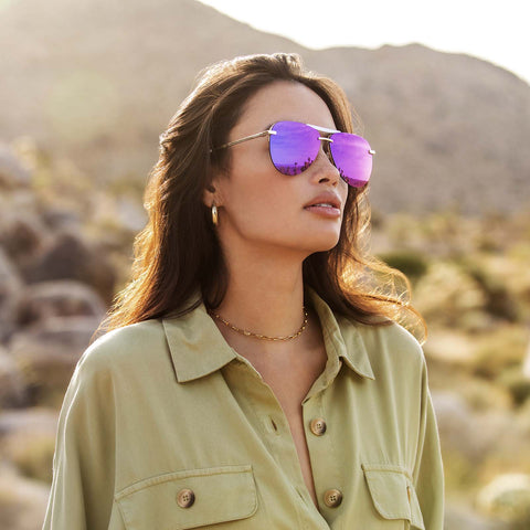 Young woman in desert wearing purple mirrored aviator glasses looking off into the distance