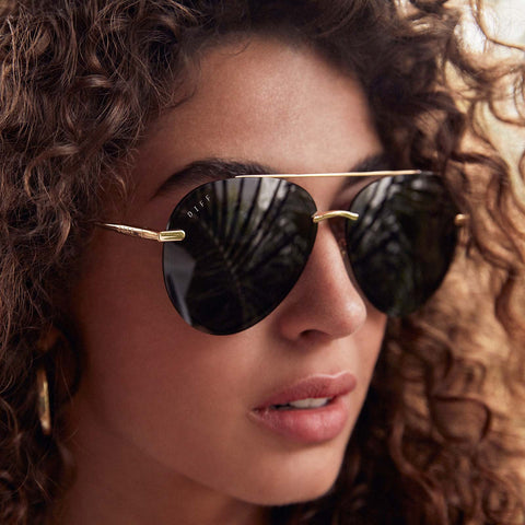 Close up portrait of woman with wavy hair looking into the distance wearing the Lenox Gold Aviator Sunglasses with blue lens