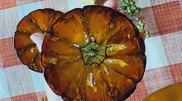 resin pumpkin coaster sitting on a hand above an orange gingham tablecloth