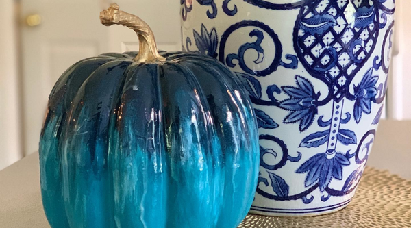 blue resin pumpkin home decor piece sitting next to a blue pattern vase on a wooden table
