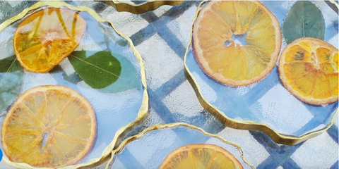 two clear epoxy resin art coasters with dried lemons and greenery inside them sitting on top of a blue picnic cloth