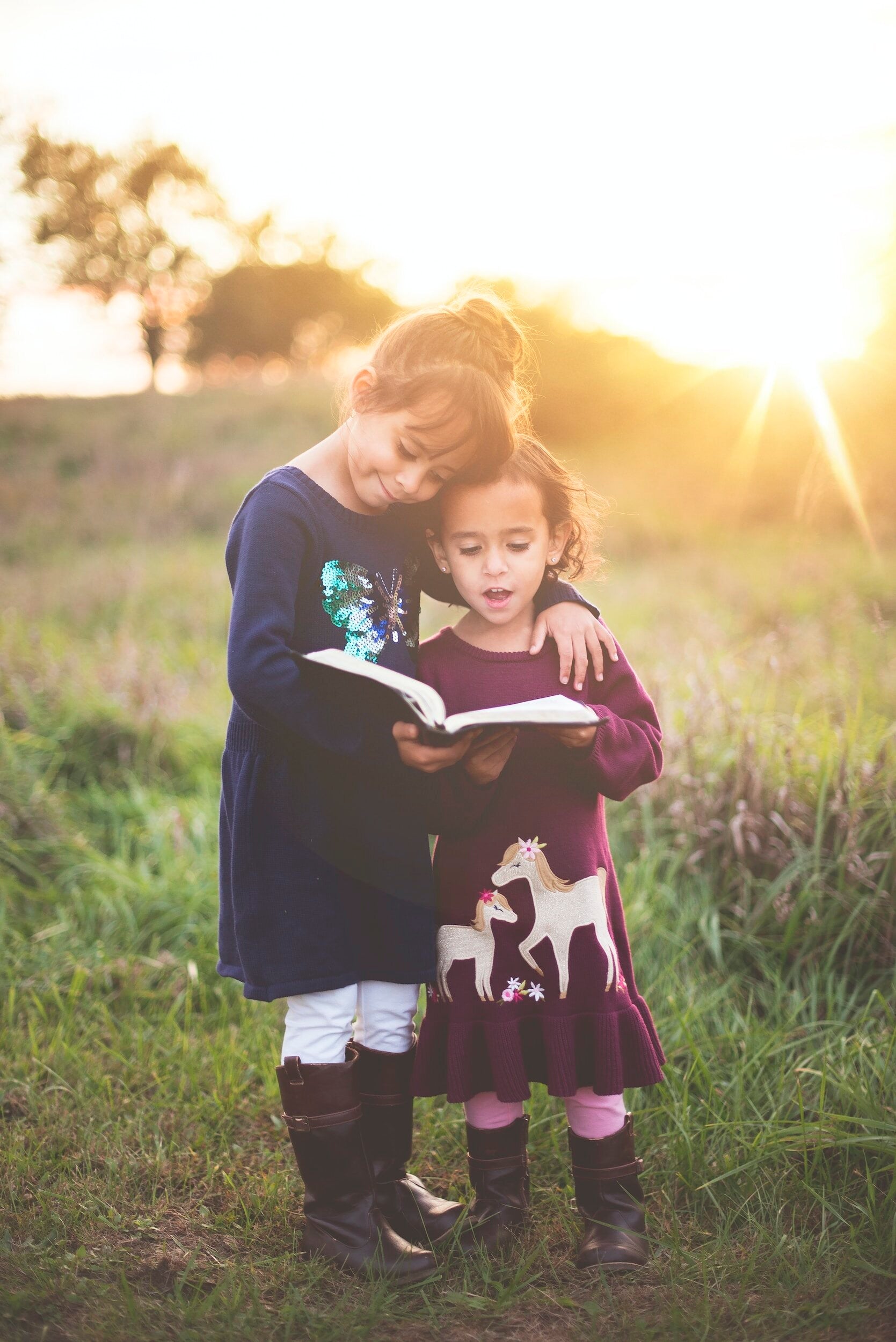 2 girls reading a book together outside at dusk