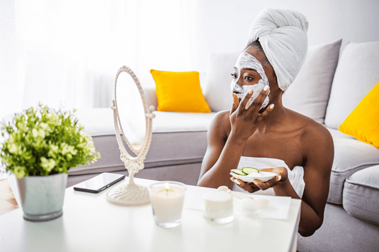woman sitting and applying a facial mask at home while wearing a bath towel  in front of the mirror
